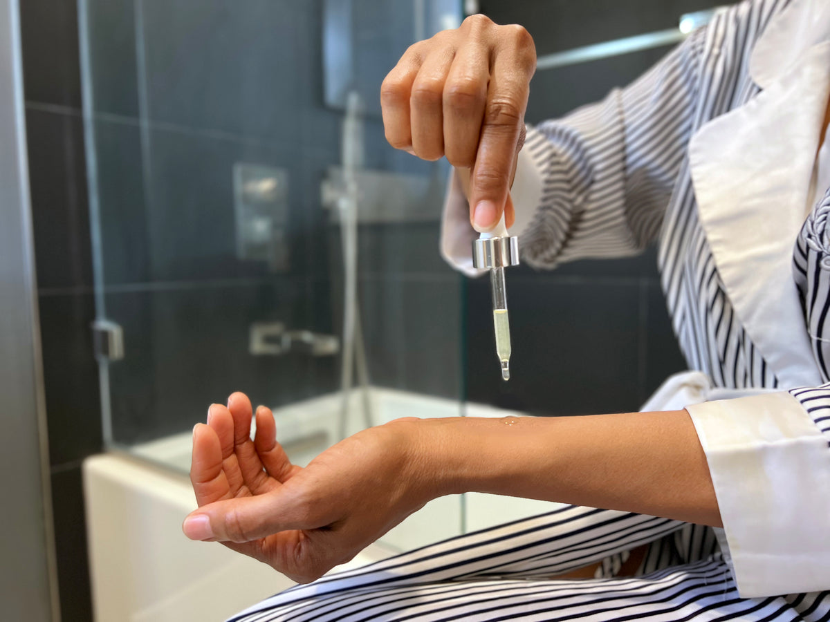 Person holding a dropper with a clear liquid in a bathroom setting